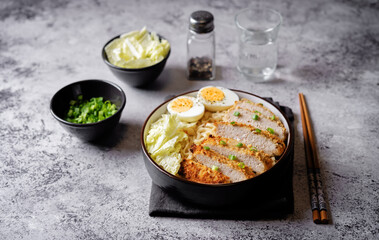 Ramen noodles with meat schnitzel slices, peking cabbage, eggs and scallions in a bowl
