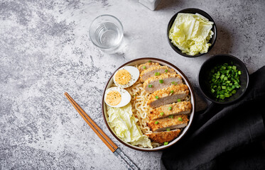 Ramen noodles with meat schnitzel slices, peking cabbage, eggs and scallions in a bowl