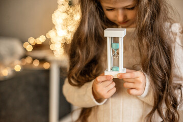 girl holding a sand watch behind the Christmas tree 