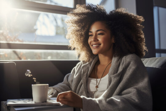 Pretty African American girl in home clothes with laptop and morning cup of coffee in cozy room. Female specialist works online, participates in conference call. Remote job concept.