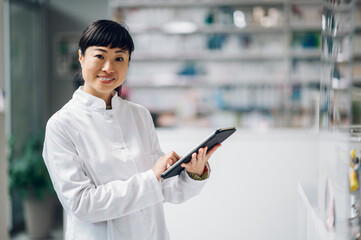 Portrait of a Japanese technician standing in a drugstore with a tablet in her hands.