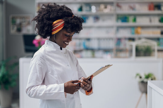 A cheerful young pharmacy worker is smiling at the clipboard while standing at her workplace.