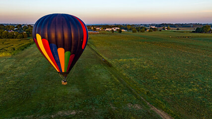 Obraz premium An Aerial View of a Black Striped Hot Air Balloon Floating Low Over Fields and Farmlands in Rural America on a Sunny Summer Morning.