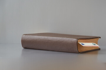 Old book with no title on the cover lies on a gray background with a bookmark of 10 euros between the pages