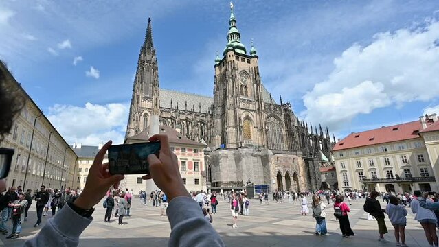Prague, Czech Republic, August 4, 2023. Slow motion footage on St. Vitus Cathedral Square. A young Caucasian man takes photos with his cell phone. Beautiful summer day, people in the square.