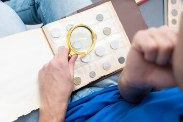 A passionate numismatist examines purchased old and ancient coins with a magnifying glass.
