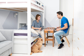 Husband and wife playing table football in children's room while their kids aren't at home