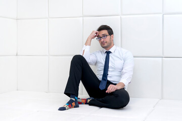 Sad and frustrated businessman in formal wear sitting in a white room in a mental hospital