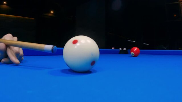 Close-up of hitting a white ball with a cue during a game of billiards. A player takes aim at a white ball while playing pool on a table with a blue cloth. Professional ball kick in billiard club. 