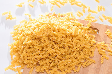 Uncooked Fusilli Pasta Scattered on Wooden Board and White Table. Raw and Dry Macaroni. Fat and Unhealthy Food
