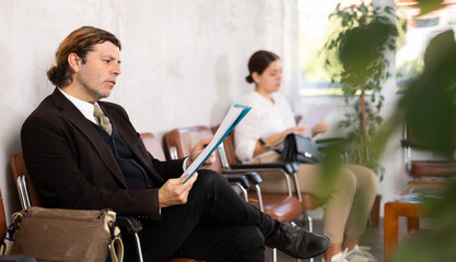 Obraz premium Unemployed man of middle age is waiting for job interview in hall. Bored male candidate for job is waiting for invitation to recruiter s office