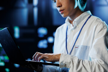 Dara center system administrator running code and programming on laptop, troubleshooting and upgrading high tech facility designed to accommodate rows of fully operational servers