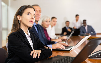 Fototapeta premium Woman sitting at table beside her colleagues during meeting in conference room and using laptop.