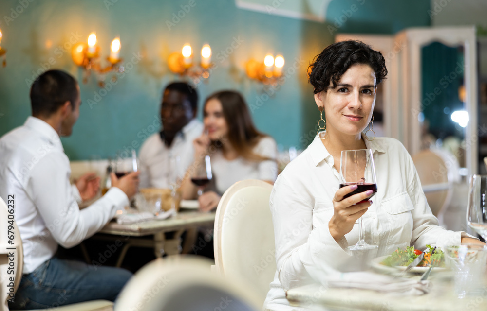 Wall mural Latino woman holding glass of red wine in cozy restaurant