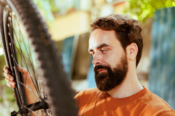 Active male cyclist checking tire as yearly bike rubber maintenance routine. Detailed image of enthusiastic sporty caucasian man gripping and examining damaged bicycle wheel for dismantle.