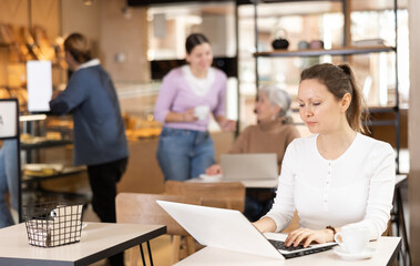 Obraz premium Confident female cafe customer enjoying peace and quiet while working on laptop