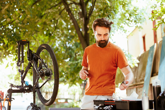 Dedicated fit and active man outside demonstrating commitment to changing and securing bicycle components for summer cycling leisure. Picture of young caucasian male arranging professional equipment