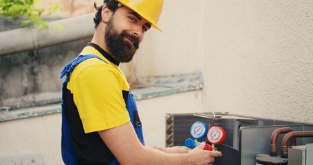 Efficient technician looking at refrigerant levels in external air conditioner while using manifold...