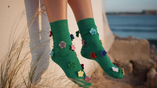 Happy girl feet dangle in colorful stylish socks closeup. Carefree kid at shore