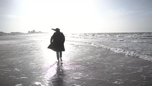 a girl in a coat walks on the beach