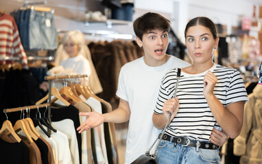 Couple in clothing shop look in surprise towards window and discuss discount promotion of store....
