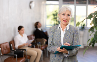 Interested positive elderly businesswoman holding folder with papers, writing tasks and...