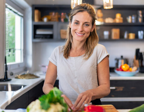 Likeable, pretty 30-as caucasian woman cooking at home in the kitchen. She looking at the camera.