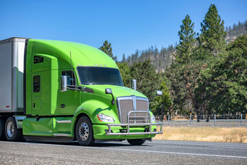 Fototapeta na wymiar Bonnet green big rig semi truck tractor transporting commercial cargo in dry van semi trailer driving on the one way mountain highway road