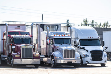 Bonnet industrial long hauler big rig semi truck tractors with semi trailers standing in row on the truck stop parking lot take a break for truck drivers rest