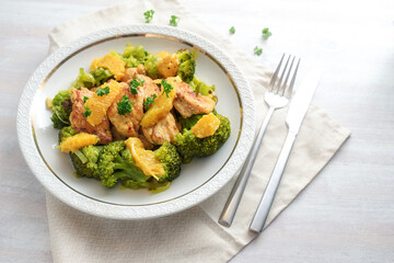 Orange chicken fillet on broccoli vegetables with parsley garnish, served on a white plate, healthy protein meal for low carb diet, copy space, selected focus, narrow depth of field
