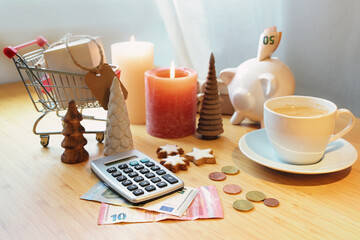 Saving money on holiday shopping, calculator, piggy bank, coins and banknotes on a table among Christmas decoration, candles and a shopping cart, copy space, selected focus