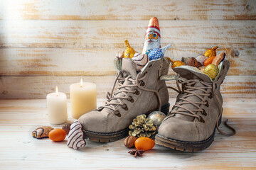Winter boots, sweets, Christmas decoration and a chocolate Santa against rustic wood, tradition on Nicholas day or in German Nikolaus Tag to fill shoes at 6th December, copy space - obrazy, fototapety, plakaty