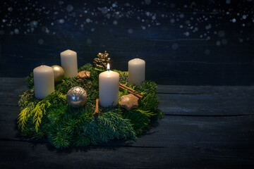 Green advent wreath with white candles, one is lit for first advent, Christmas decoration and cookies, dark blue wooden background with star bokeh, copy space