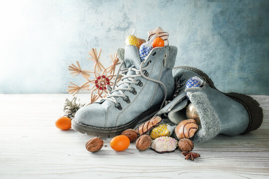 Nicholas day or in Germany Nikolaus Tag in December, winter boots filled with treats and Christmas decoration against a cold blue gray background, copy space, selected focus