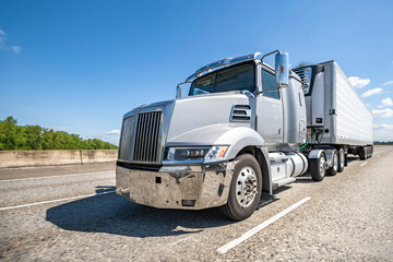 Light gray stylish day cab big rig semi truck tractor transporting cargo in reefer semi trailer...