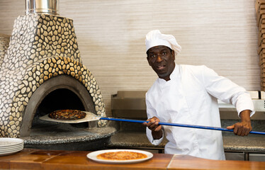 Portrait of stressed pizza chef at work, emotional man taking burned pizza from oven at pizzeria...