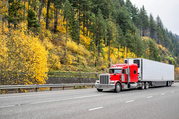 Red classic long hauler American big rig semi truck transporting frozen cargo in loaded reefer semi trailer driving on the autumn highway road in Columbia River Gorge - obrazy, fototapety, plakaty