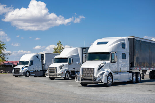 Three white big rig industrial semi trucks with semi trailers standing on rest area parking lot take a break