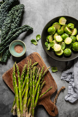 raw organic asparagus, kale and Brussels sprouts on a table, grey background, top view, healthy...