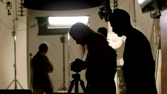 Silhouettes of people in a photo studio. The preparation of equipment for the photoshoot involves configuring cameras, lighting, and other technical aspects to achieve the desired visual effects.