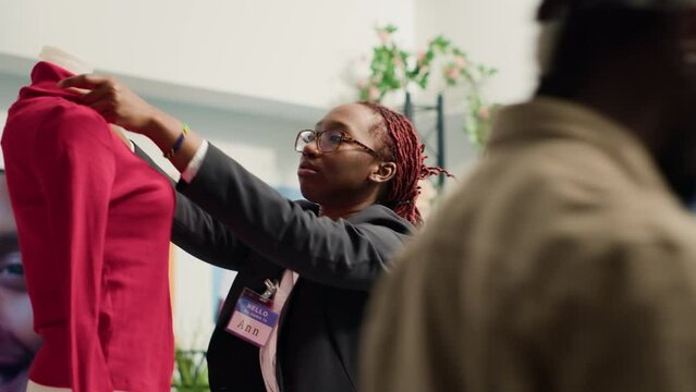 Woman tidying up luxury fashion boutique elegant clothes on mannequin. African american worker removing creases from new season high class garments in trendy clothing store