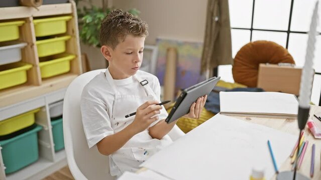 Adorable blond boy artist focused on drawing art on touchpad in the relaxing environment of a studio class