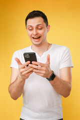 young man holding a phone, talking emotionally on the phone on a yellow background.