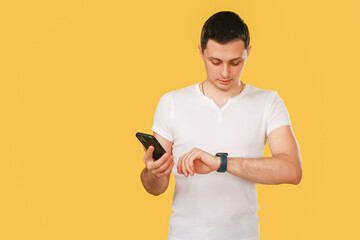 man looking at watch and phone on yellow.