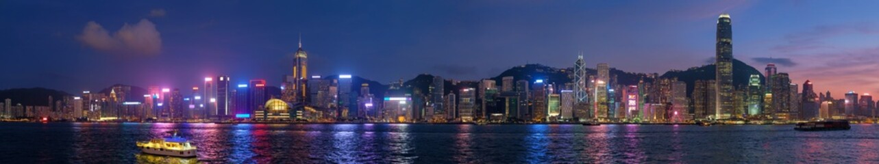 Panorama of Hong Kong skyline cityscape downtown skyscrapers over Victoria Harbour in the evening illuminated tourist boats and ferries . Hong Kong, China