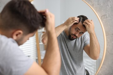 Man with dandruff in his dark hair near mirror in bathroom - obrazy, fototapety, plakaty