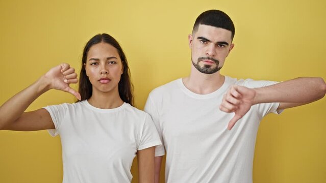 Uncool vibes &ndash; beautiful couple together, seriously thumbs-down, against a strikingly yellow isolated wall