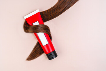 Hair cream bottle wrapped in hair lock on beige background, flat lay with space for text. Natural...