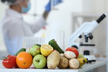 Fresh vegetables, fruits on table and scientist proceeding quality control in laboratory