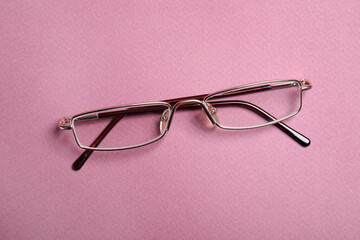 Stylish pair of glasses with metal frame on pink background, top view